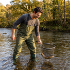 Angler in chest waders netting a trout in a British river