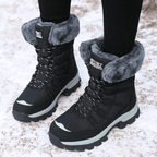 Women's winter boots in Black with a grey faux fur cuff, worn in the snow