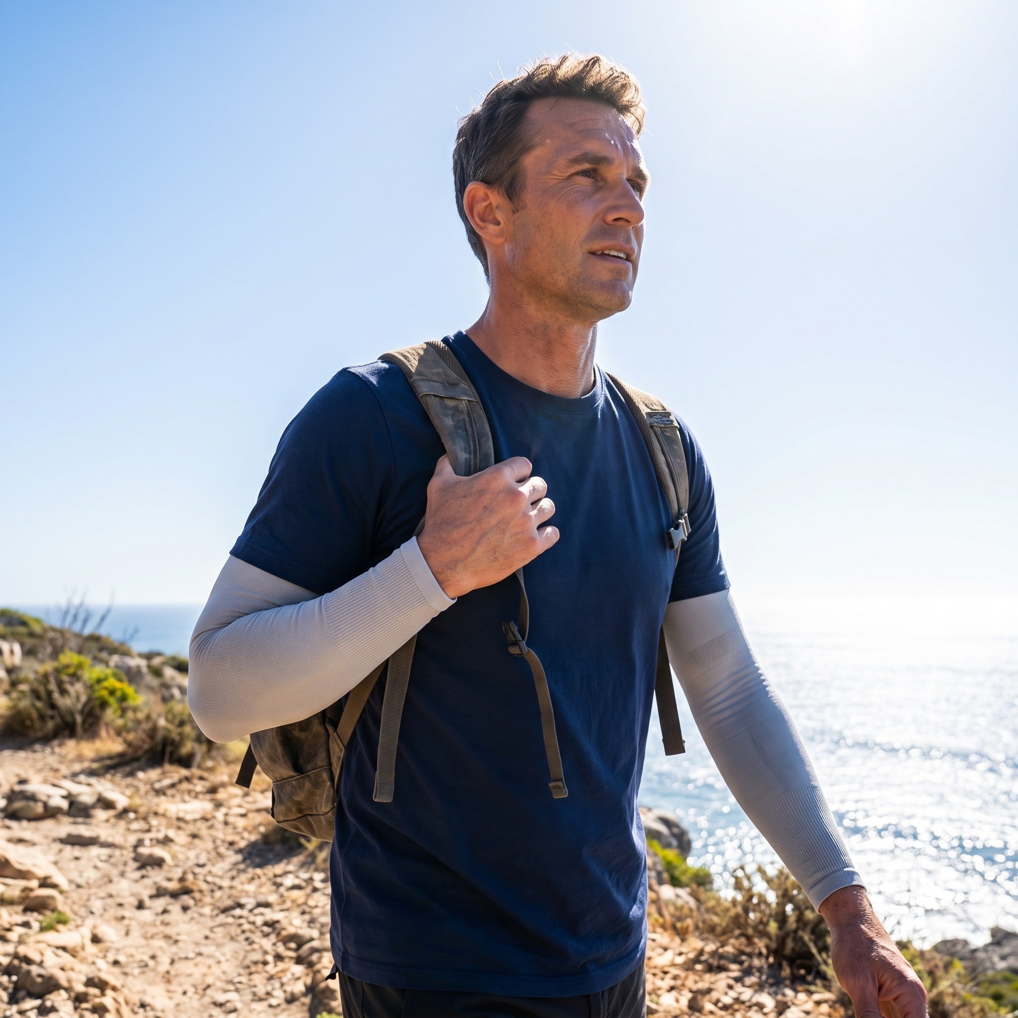Man walking a sunlit coastal path wearing UPF 50+ arm sleeves