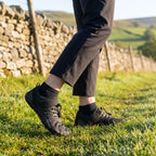 Black barefoot shoes worn on a grass footpath beside a dry-stone wall