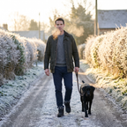Man walking a black Labrador along a frosty village lane in Britain at first light in fur lined winter boots