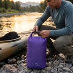 Paddler sealing a dry bag beside a kayak