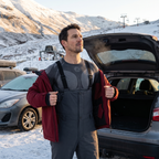 Man pulling a ski jacket on over the black base layer top and salopettes in a ski centre car park in Scotland
