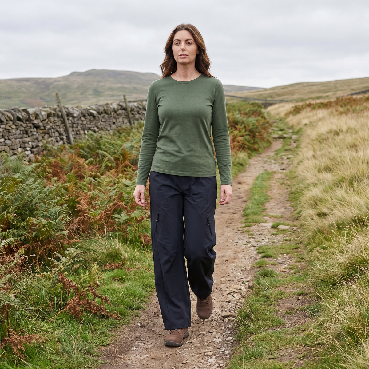A woman walking a British upland path in the women's wide leg walking trousers, dry stone wall and bracken beside the track