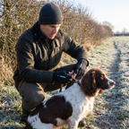 Man clipping a lead onto a springer spaniel on a frosty English footpath wearing the flip finger gloves