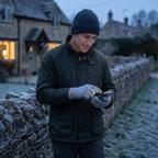 Man using his phone with knitted gloves on in an English village at dusk