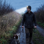 Man walking a spaniel on a country lane in England at dusk wearing the head torch, lead in one hand and a bag in the other
