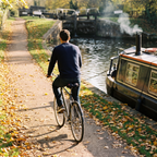 Man riding a city bike along a canal towpath with the padded seat cover on his saddle