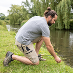 Man kneeling on a riverbank in Britain wearing the Khaki cargo shorts