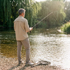 Angler on a sunny riverbank wearing the men's fishing shirt in Khaki, seen from behind