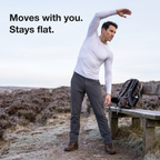 Man stretching one arm overhead on a frosty moorland path in Britain, the white base layer top moving with him and its hem staying down