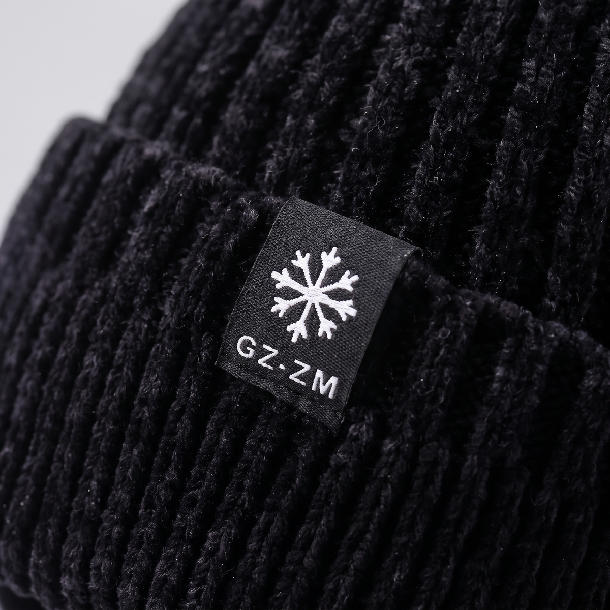 Close-up of the double-layer turn-up cuff and woven snowflake label on the black winter hat