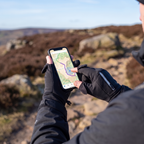 Walker in the Peak District tapping a map on a phone with a bare fingertip, glove caps folded back