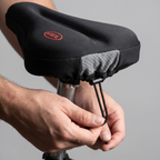 Hands pulling the drawstring tight under the saddle to fix the bike seat cover in place
