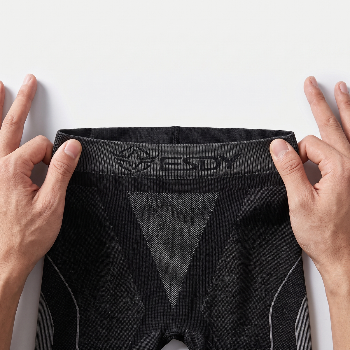Hands stretching the wide knitted ESDY logo waistband of the black base layer leggings