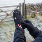 Walker opening the zip cuff to pull a glove on beside a field gate