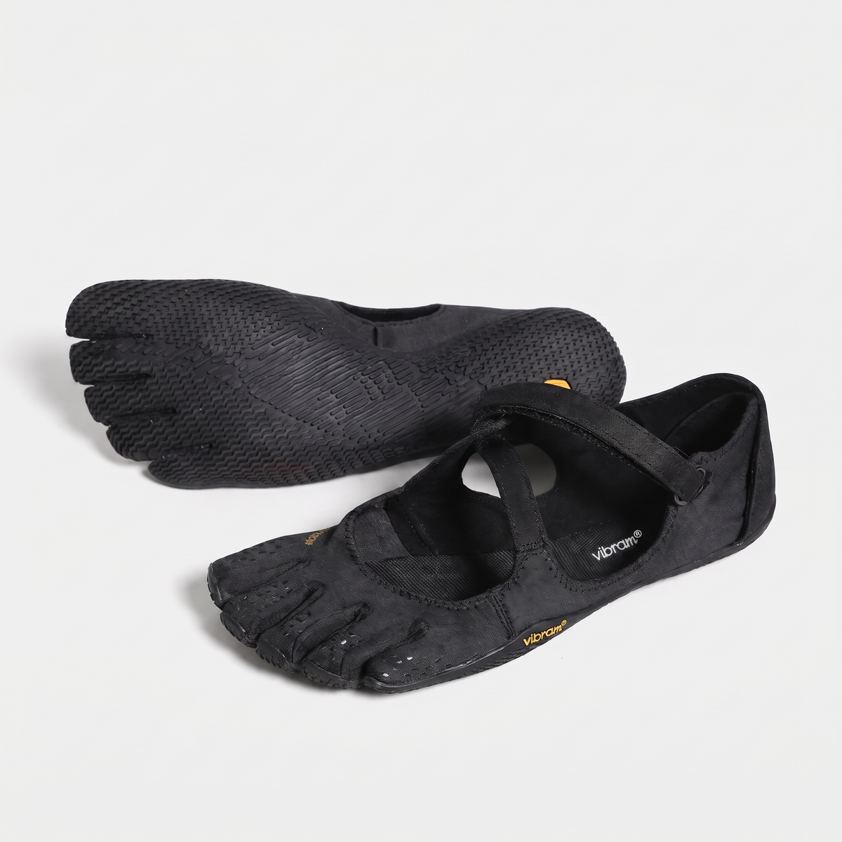 Women's barefoot five toe shoes in black, a pair with one sole turned up to show the toe pads