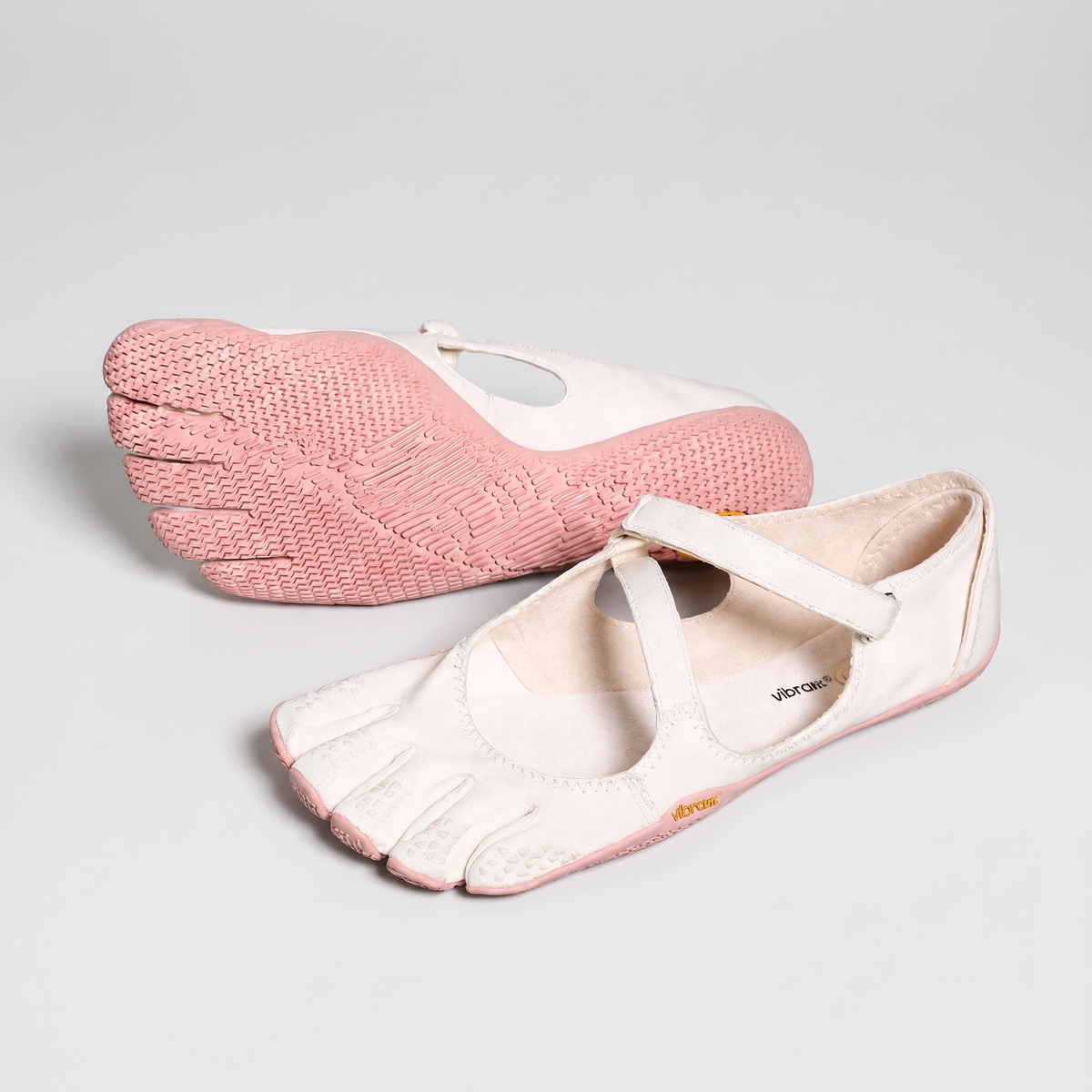 Women's barefoot five toe shoes in pink, a cream shoe on a pink sole, one sole turned up