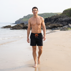 Man walking on a Cornish beach in black men's swim shorts