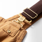 Close-up of the adjustable strap webbing and brass slider buckle on the canvas dungarees