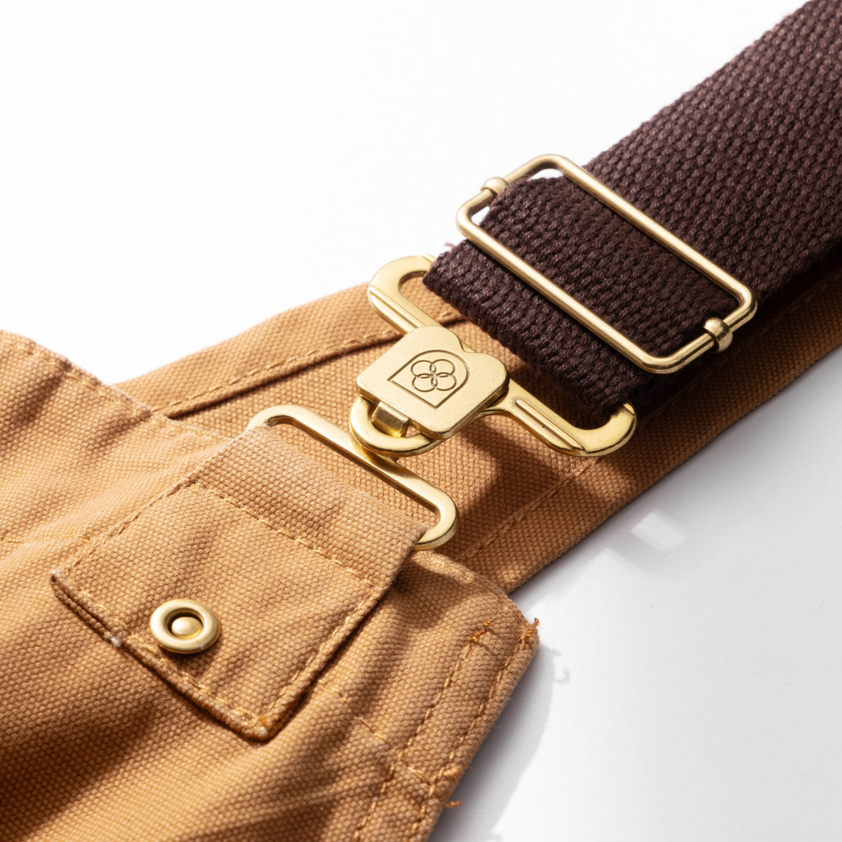 Close-up of the adjustable strap webbing and brass slider buckle on the canvas dungarees