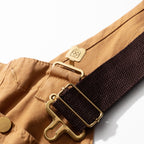 Brass buckle hook fastening the crossback strap to the bib of the canvas dungarees
