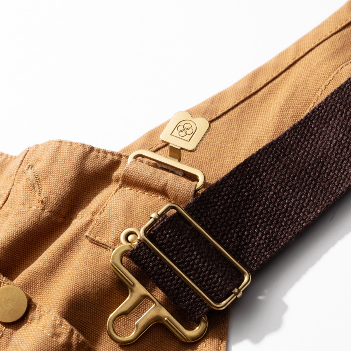Brass buckle hook fastening the crossback strap to the bib of the canvas dungarees