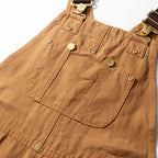Bib front of the camel canvas dungarees showing the snap chest pocket and buckle straps