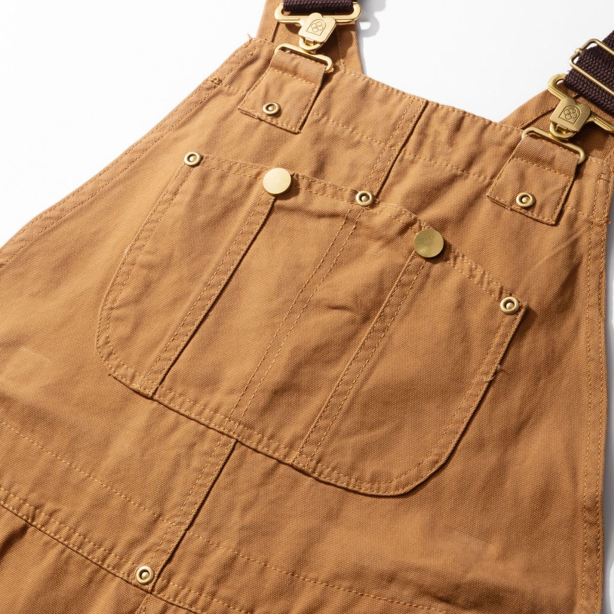 Bib front of the camel canvas dungarees showing the snap chest pocket and buckle straps