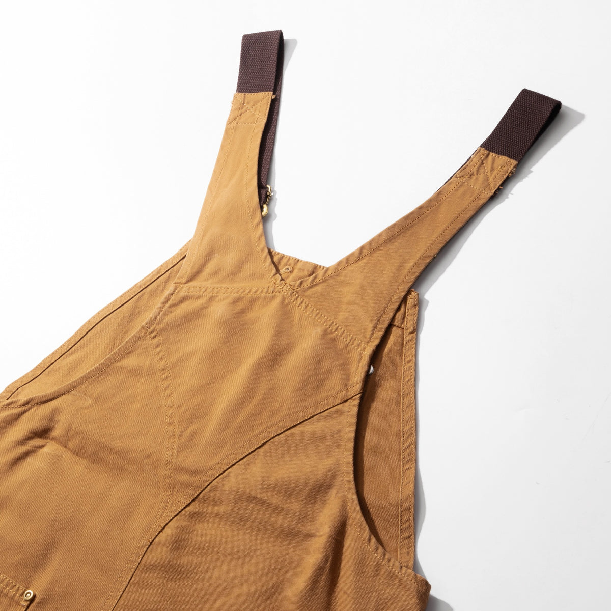 Side of the camel canvas dungarees showing the strap over the shoulder and the curved side seam
