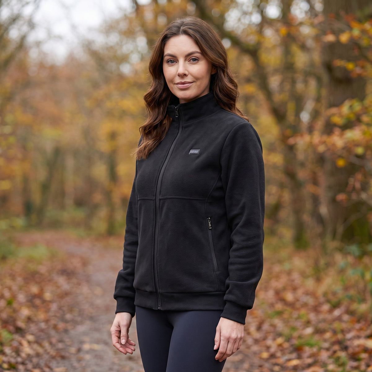 Heated fleece jacket worn by a woman, three-quarter view on a woodland path
