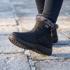 Black winter boot mid-step on frosted paving with the tread showing