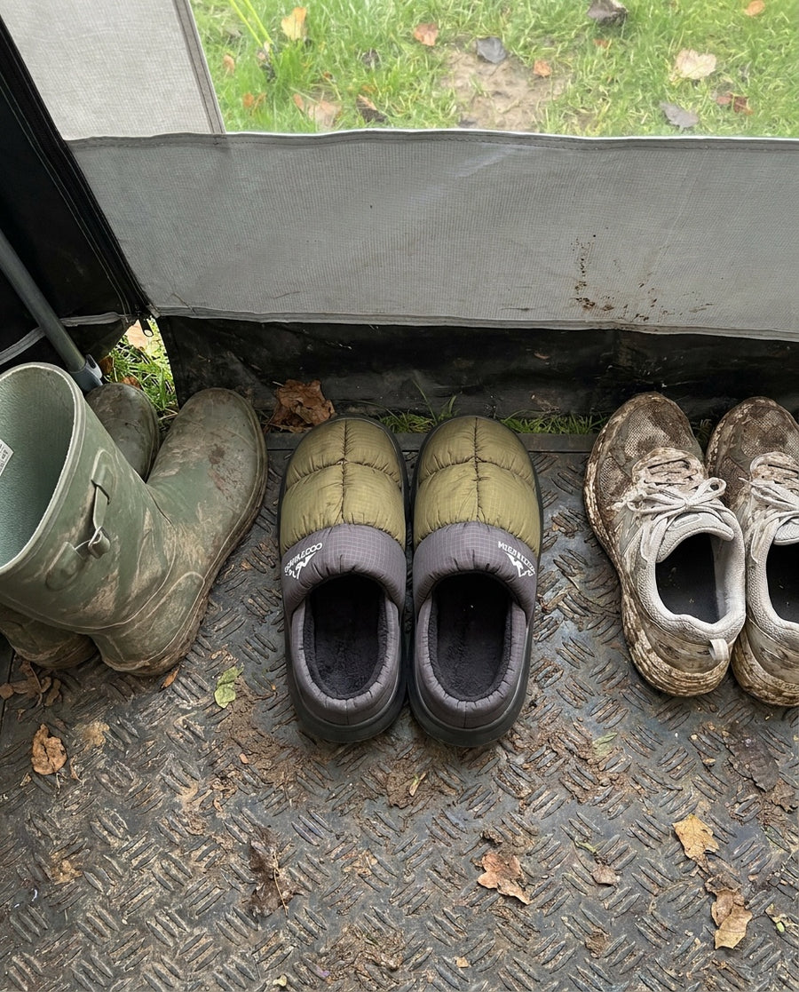 Wellies, muddy trainers and a pair of Terrabound Camp Slippers lined up on a mat in a tent awning