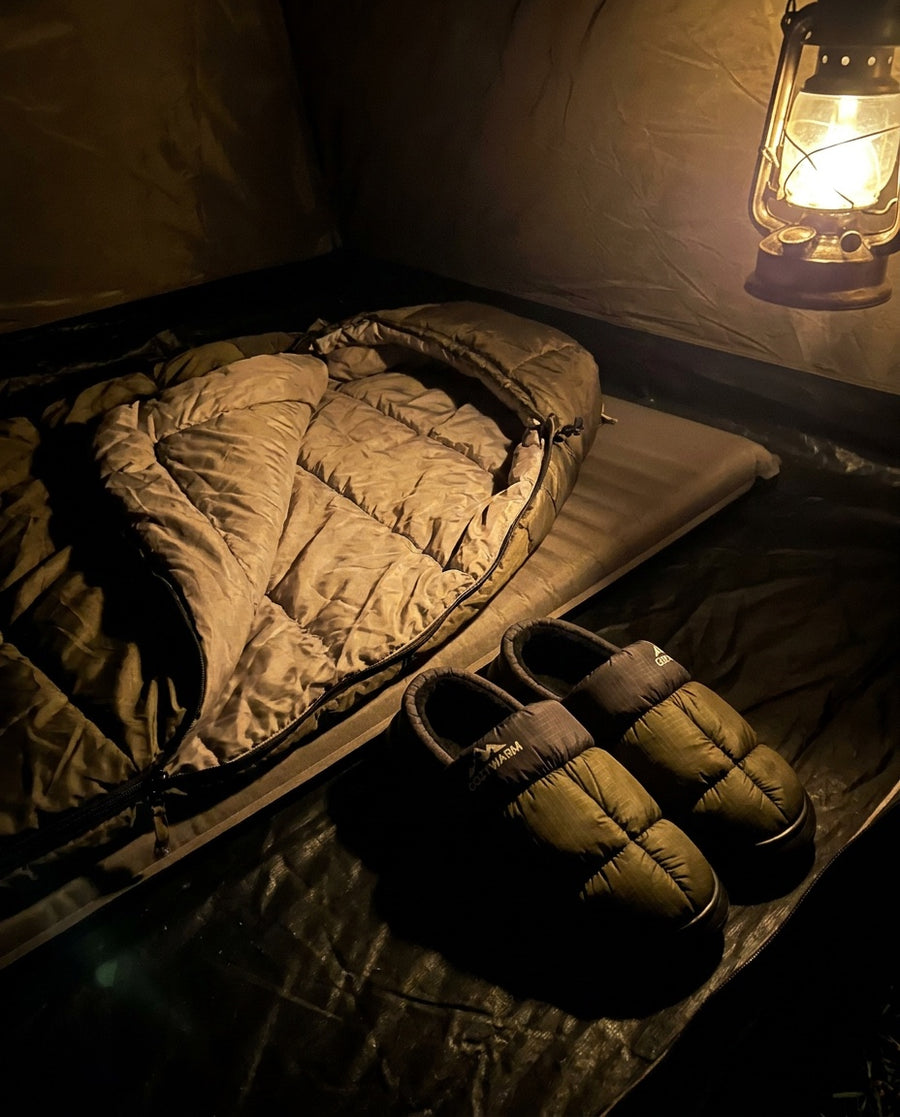 Terrabound Camp Slippers beside an open sleeping bag in a tent lit by a lantern