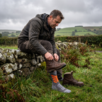 A walker lacing a boot on a drystone wall, the crew sock visible on the other foot