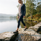 Woman stepping between lakeside rocks wearing black five toe barefoot shoes