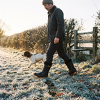 Man walking a springer spaniel across a frosty field at sunrise in fleece lined wellies