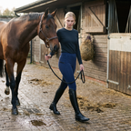 Woman leading her horse across a stable yard wearing navy two-tone pull-on jodhpurs
