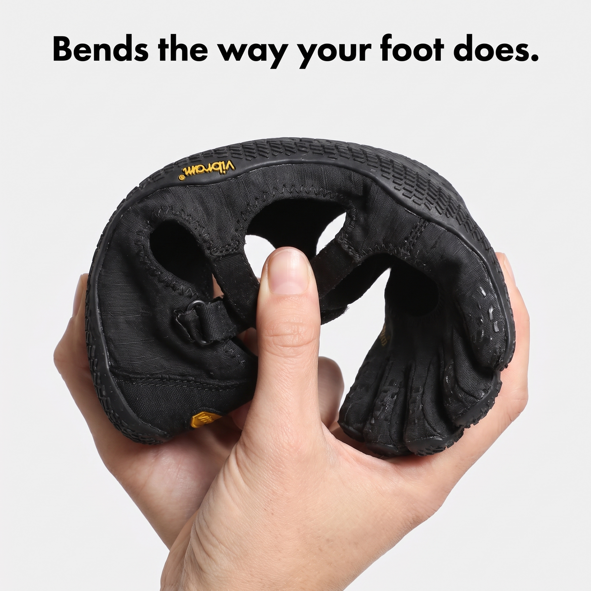 Hand bending a black five toe shoe to show the thin, flexible sole