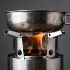 Camping pan resting on the toothed pot arms of the wood burning stove