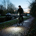 Rider on an unlit canal towpath at dusk with the front bike light lighting the path