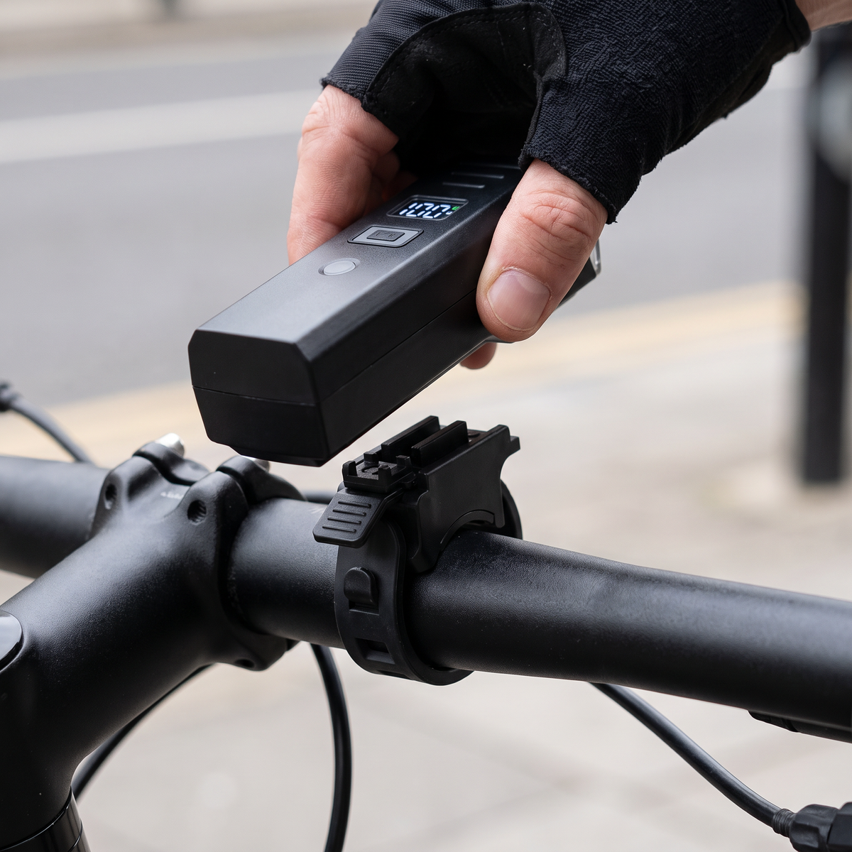 Gloved hand lifting the bike light off its quick-release bracket, the strap left on the handlebar