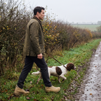 Man walking a spaniel in side zip walking boots along a muddy field edge