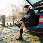 Man lacing a walking boot at a frosty trailhead, wearing black merino wool knee high socks