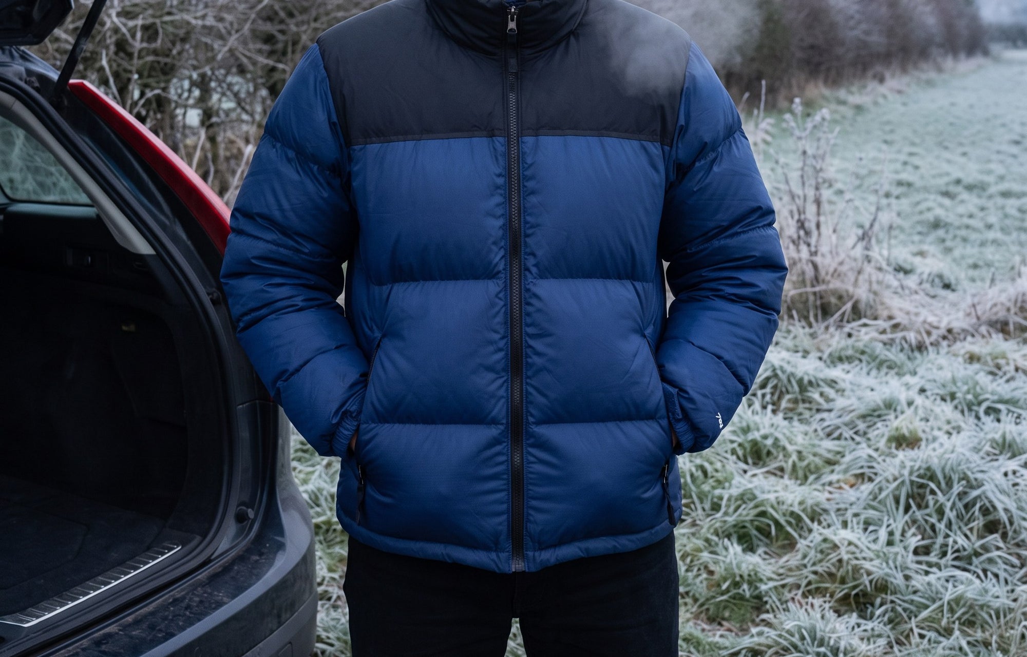 Man standing at an open car boot on a frosted verge in the Navy Terrabound colour block puffer jacket, hands in the pockets