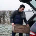 Man in the Navy down gilet lifting a crate into a car boot on a frosted verge