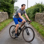 Cyclist riding a gravel bike on a UK country lane wearing the Royal Blue cycling shorts with a water bottle in the lower back pocket