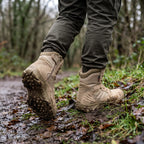 Khaki combat boots stepping onto a muddy woodland bank
