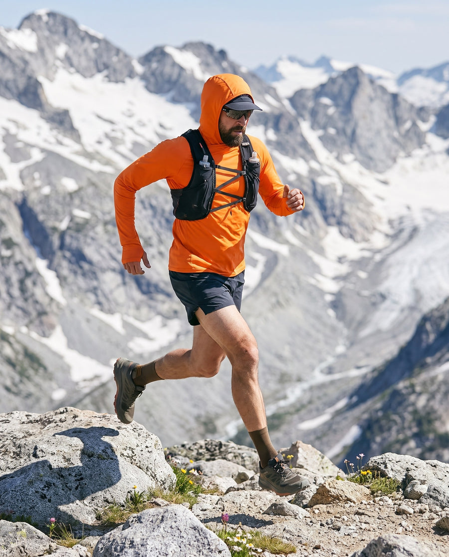 Trail running in the orange sun hoodie, hood up over a cap, high mountains behind