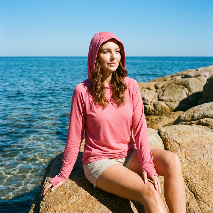 Woman sitting on coastal rocks in the rose sun hoodie with the hood up